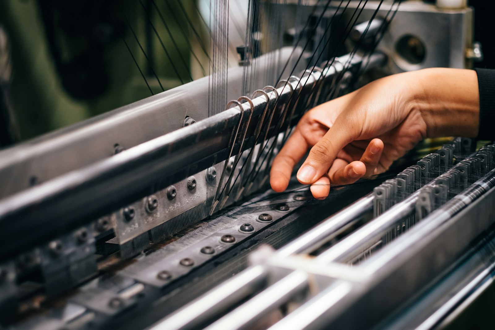 Close-up of hands guiding warp threads through a weaving loom.